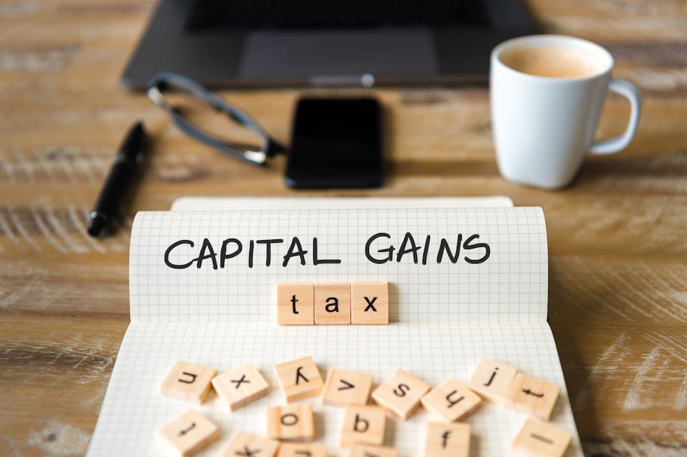Image of paper on a table with capital gains written in inked pen with tax spelt using scrabble pieces.